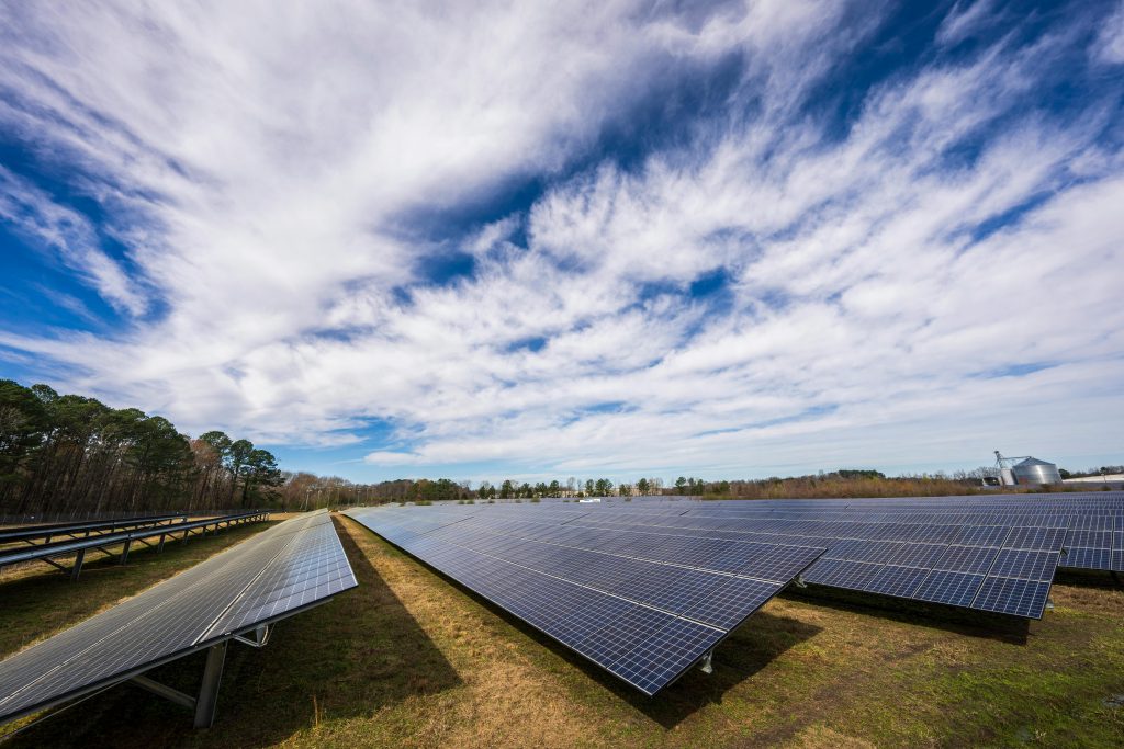 Solar panels spread across a field under a bright blue sky with clouds, showcasing renewable energy.